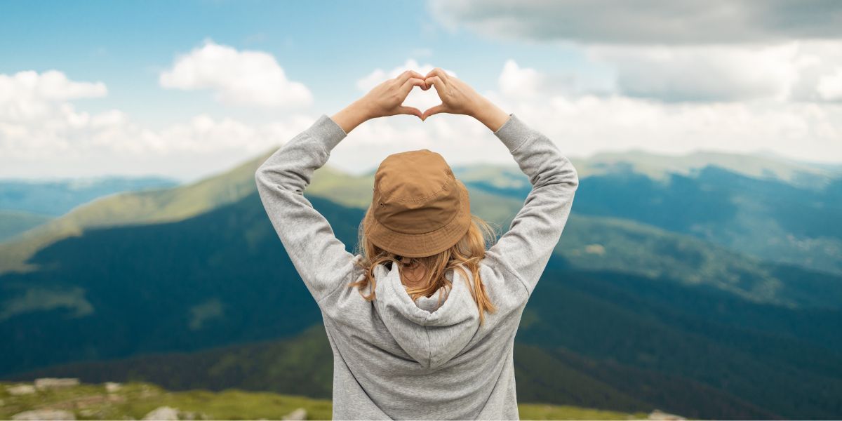 Woman standing on top of a mountain making heart shape with her hands